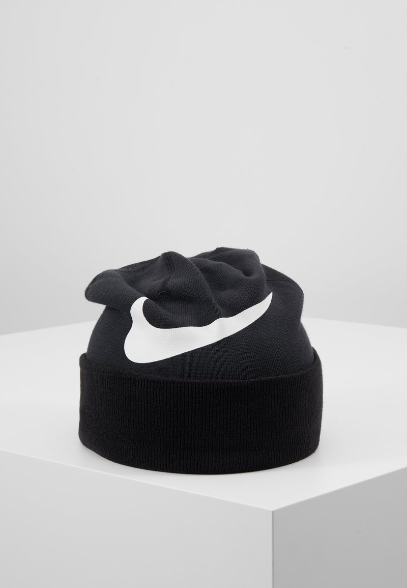 Zwart gebreide beanie met een omgevouwen manchet, voorzien van een opvallend wit Nike-logo aan de voorkant. Zachte textuur, ronde vorm.