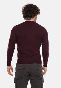 Suéter de punto burdeos con mangas largas, diseño ajustado y puños acanalados. Textura suave, cuello redondo y sin herrajes o patrones visibles.