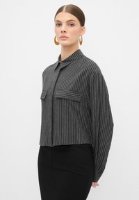 Grijs gestreept cropped shirt met een kraag en twee voorzakken, gemaakt van zachte stof; gecombineerd met een strakke zwarte rok.