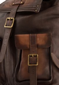 Bruine leren rugzak met een groot hoofdvak, een voorvak, messing hardware en een contrasterende textuur door versleten delen.