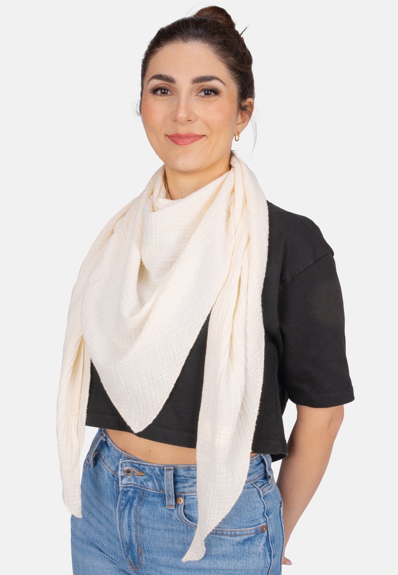 Écharpe blanche texturée drapée autour du cou, présentant une forme triangulaire et un tissu doux, assortie à un haut noir à manches courtes et à un jean.