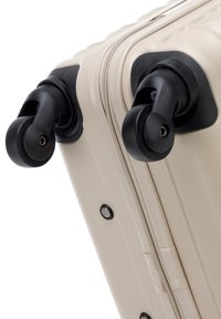 Dos ruedas giratorias negras sujetas a la esquina de una maleta rígida beige con una cremallera visible.