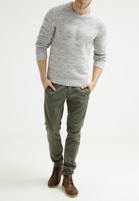 Pull gris clair en maille avec un motif texturé, pantalon vert olive et bottines en cuir marron. Ensemble décontracté avec une coupe ample.