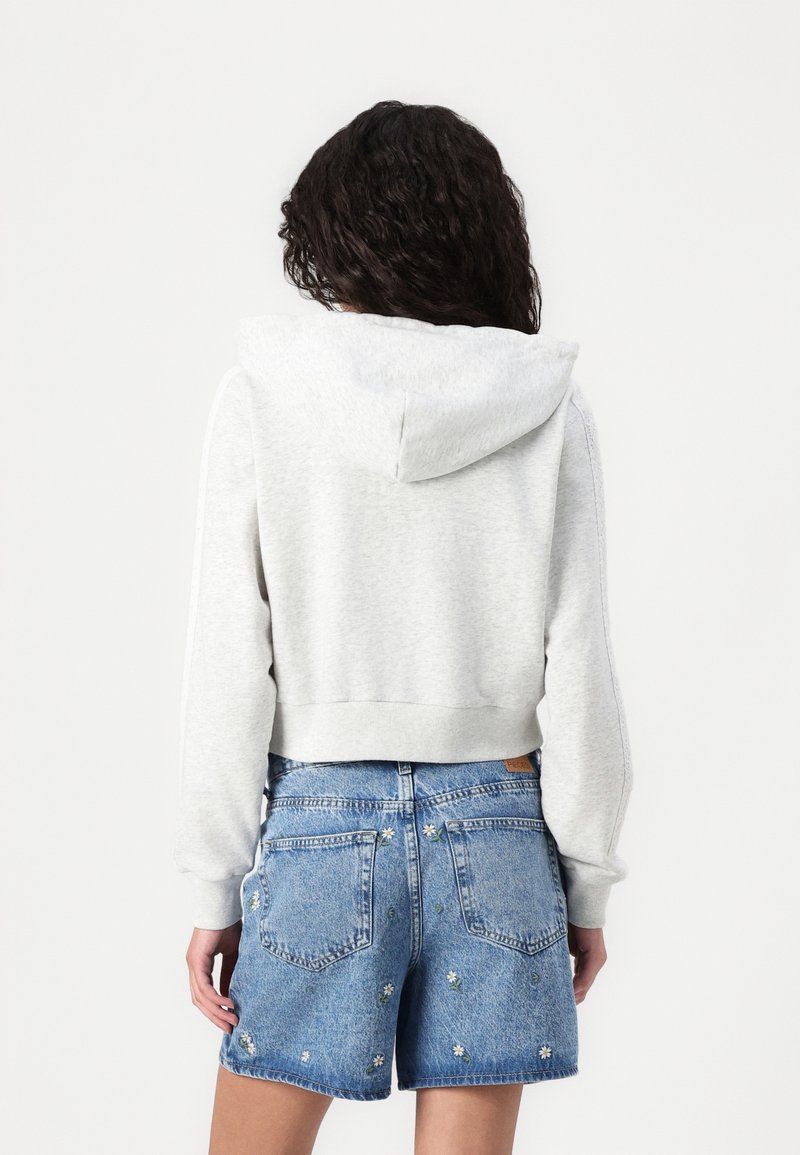 Hoodie grigia corta con cappuccio, abbinata a pantaloni shorts di jeans blu con ricami floreali sulle tasche. Texture liscia, design casual.