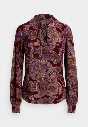 Blouse bordeaux à manches longues avec un motif cachemire en violet, or et blanc. Présente un col à lacer et des poignets froncés.