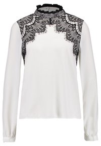 Blouse blanche à manches longues. Superposition de dentelle noire détaillée aux épaules, col montant avec bordure à volants. Texture de tissu lisse.