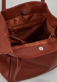 Bruine leren tote bag met een gestructureerde buitenkant, een gladde binnenvoering, een ritsvak en een magneetsluiting.