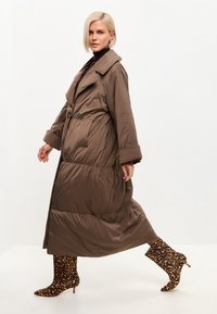 Cappotto puffo marrone con colletto e tasche laterali, caratterizzato da una vita stretta e una silhouette fluida, abbinato a stivaletti alla caviglia con stampa leopardata.