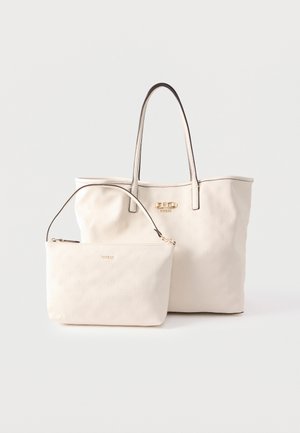 Deux sacs Guess couleur crème : un grand cabas avec doubles poignées et un petit sac à main zippé avec une seule bandoulière, tous deux embossés de logos.