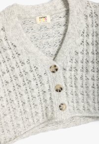 Cardigan a maglia grigia chiara con scollo a V, caratterizzato da un motivo testurizzato, tre bottoni beige e una consistenza morbida e pelosa.