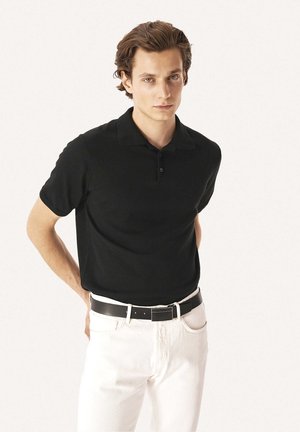 Sort polo skjorte med korte ærmer, tekstureret stof og krave. Kombineret med hvide denim bukser og et sort bælte. Enkel design.