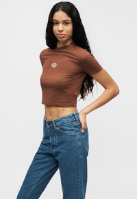 T-shirt marron court avec manches courtes et col rond; arborant un logo multicolore sur la poitrine; associé à un jean bleu taille haute.