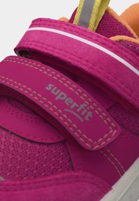 Κοντινό πλάνο ροζ παιδικού παπουτσιού με δύο λουράκια βέλκρο, το ένα με ετικέτα «superfit», και πορτοκαλί εσωτερική επένδυση.