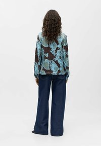 Patterned shirt in blue and brown with long sleeves, paired with wide-leg dark denim jeans, viewed from the back. Textured surface visible.