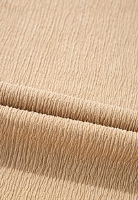 Tissu beige avec un motif texturé côtelé, présenté plié pour mettre en valeur ses détails linéaires doux et en relief.