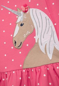 Rotes Kleid mit einem Einhorn-Design, das ein beiges Gesicht, eine weiße Mähne, einen silbernen Horn und eine pinkfarbene Blütenakzent auf der linken Seite zeigt. Weiße Polka-Dots überall.