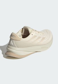 Beige sportieve schoen met een ademende mesh bovenkant, strak ontwerp, gestructureerd oppervlak en een gebogen zool met subtiele merkdetails.