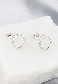 Orecchini a cerchio in argento con design circolare, caratterizzati da un piccolo accento in pietra preziosa sulla chiusura. Texture liscia, stile minimalista.