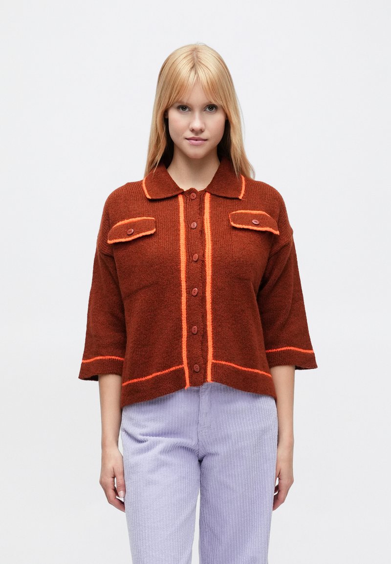 Pruun lühendatud kampsun kraega, oranži äärega ja kahe rinnataskuga. Omab viit nööpi, kolmveerandpikki varrukaid ja tekstuurse mustriga kudumit.