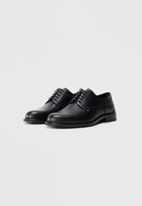 Scarpe in pelle nera con una finitura liscia e dettagli texturizzati. Presentano un design tradizionale con lacci e un tacco basso impilato.
