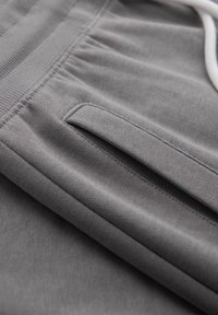 Grijze sportshorts van zacht materiaal met een elastische tailleband, voorzien van een vlakke zakdetail en een witte trekkoord. Gladde textuur.