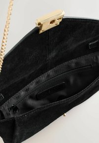 Black suede handbag interior featuring a gold frame clasp, zippered pocket, and smooth satin lining. Simple design with no visible patterns.