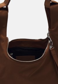 Sac à main en nylon brun avec une ouverture zippée et des accessoires en métal argenté, poche intérieure zippée et texture lisse. Sangle ajustable incluse.