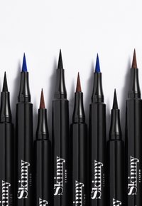 Set di otto eyeliner liquidi neri con punte a cono, disponibili in una gamma di colori che includono blu, nero e marrone. Ognuno riporta la scritta "Skinny" sul lato.