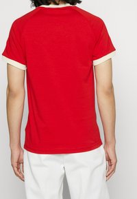 Červené tričko s krátkým rukávem, s krémovými lemy na rukávech a výstřihu, vyrobené z měkkého materiálu, s jednoduchým, klasickým designem.