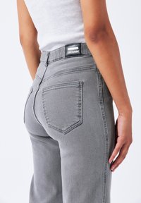 Grijze spijkerbroek met een hoge taille, met achterzakken en een zwart leren label op de tailleband. De textuur is glad en aansluitend.