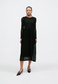 Black midi dress featuring a textured, ribbed design with long sleeves and a flared skirt. Paired with pointed black shoes.