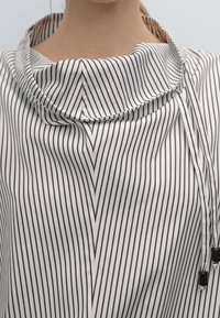 Weißes und marineblau gestreiftes Shirt mit Wasserfallausschnitt, glatter Stoffstruktur und verstellbaren Kordeln mit schwarzen Metallakzenten.