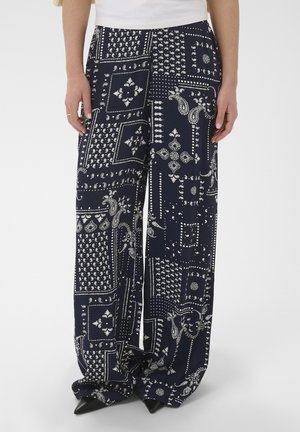 Woman wearing navy wide-leg pants with white paisley and dot patterns, paired with black pointed shoes and a white top.