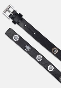 Svart läderbälte med en rektangulär silverspänne, med silveröglor och cirkulära detaljer längs remmen. Strukturert yta.