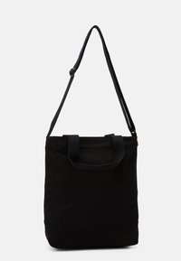 Svart kanvas tote bag med dubbla handtag och en justerbar axelrem, med en strukturerad form och en slät yta.