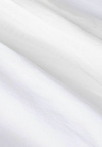 Tissu blanc avec une texture lisse et douce, présentant des variations et plis subtils, indiquant un matériau léger.