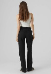 Jeans anchos negros de tiro alto, con dos bolsillos traseros y un acabado limpio. Llevado con una camiseta sin mangas de canalé blanca y sandalias.