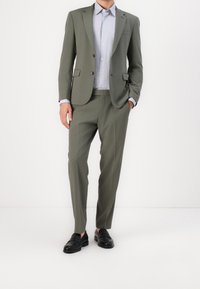 Ljusgrön skräddarsydd kostym med slim-fit design, matchande byxor och en ljusblå skjorta. Svarta loafers kompletterar outfiten.