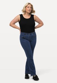 Top sin mangas negro combinado con jeans de denim azul, con un corte clásico y bolsillos frontales, complementado con zapatos negros con un acento decorativo.