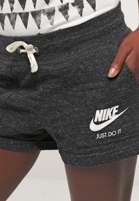 Grå shorts i texturerat tyg med resår i midjan, med en vit Nike-logotyp och "JUST DO IT" tryckt på sidan.