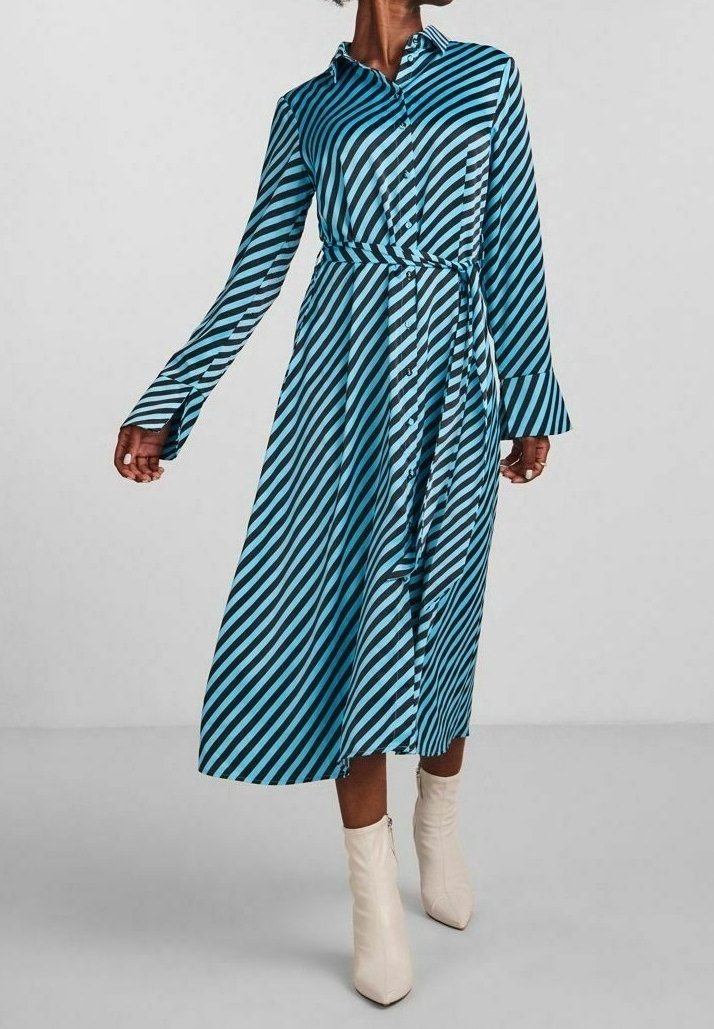 Femme portant une robe midi à manches longues rayée en diagonale bleu et noir avec une ceinture, associée à des bottines blanches.