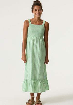 Grün-weiß gestreiftes Kleid mit gerafftem Oberteil, quadratischem Ausschnitt und gerafftem Saum. Kombiniert mit braunen Sandalen und einem perlenverzierten Knöchelarmband.