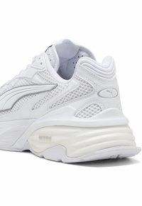 Weißer Sportschuh mit einer strukturierten Mesh-Oberfläche, gepolstertem Schaft, schlankem Design und einer gepolsterten Sohle mit dezenten Markenakzenten.