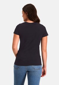 Zwart t-shirt met korte mouwen en een ronde hals, gemaakt van soepele stof, met een getailleerd ontwerp en een licht gebogen zoom, gecombineerd met blauwe denim.