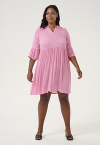 Robe rose à hauteur des genoux avec décolleté en V et manches volantes, fabriquée en tissu léger. Présente un design évasé avec une texture subtile.