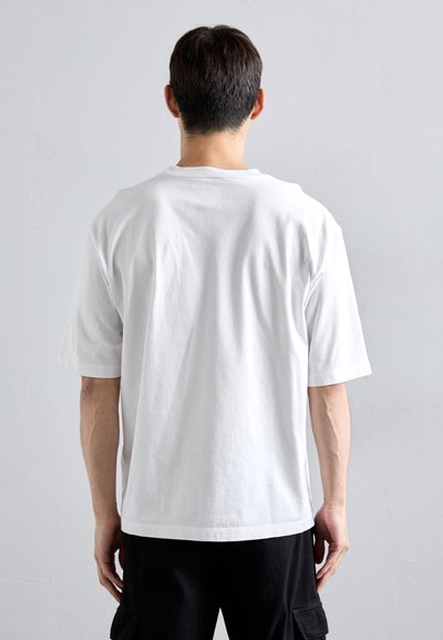 Hvid bomulds t-shirt med korte ærmer og en afslappet pasform, der har en rund halsudskæring og en glat overflade, set fra ryggen.