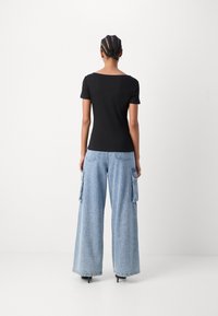 Top negru cu mânecă scurtă și blugi cargo de culoare bleumarin deschis, cu pantaloni largi și buzunare laterale. Textură netedă și croială lejeră. Pantofii cu toc completează look-ul.