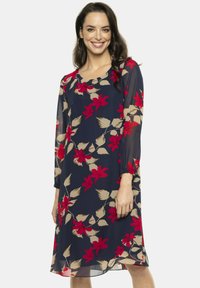 Granatowa sukienka w kwiaty z długim rękawem, z czerwonymi i beżowymi kwiatami, okrągłym dekoltem oraz zwiewnym, lekkim materiałem.