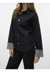 Mörk denimskjorta med grå kontrastmanschetter, knapplist fram, rak passform och rundad nederkant. Tyget visar lätt textur och sömnadsdetaljer.