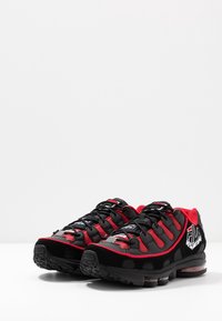 Baskets de sport noires et rouges avec une tige en maille et synthétique, semelle en caoutchouc, détails texturés et logo bien visible sur le côté.